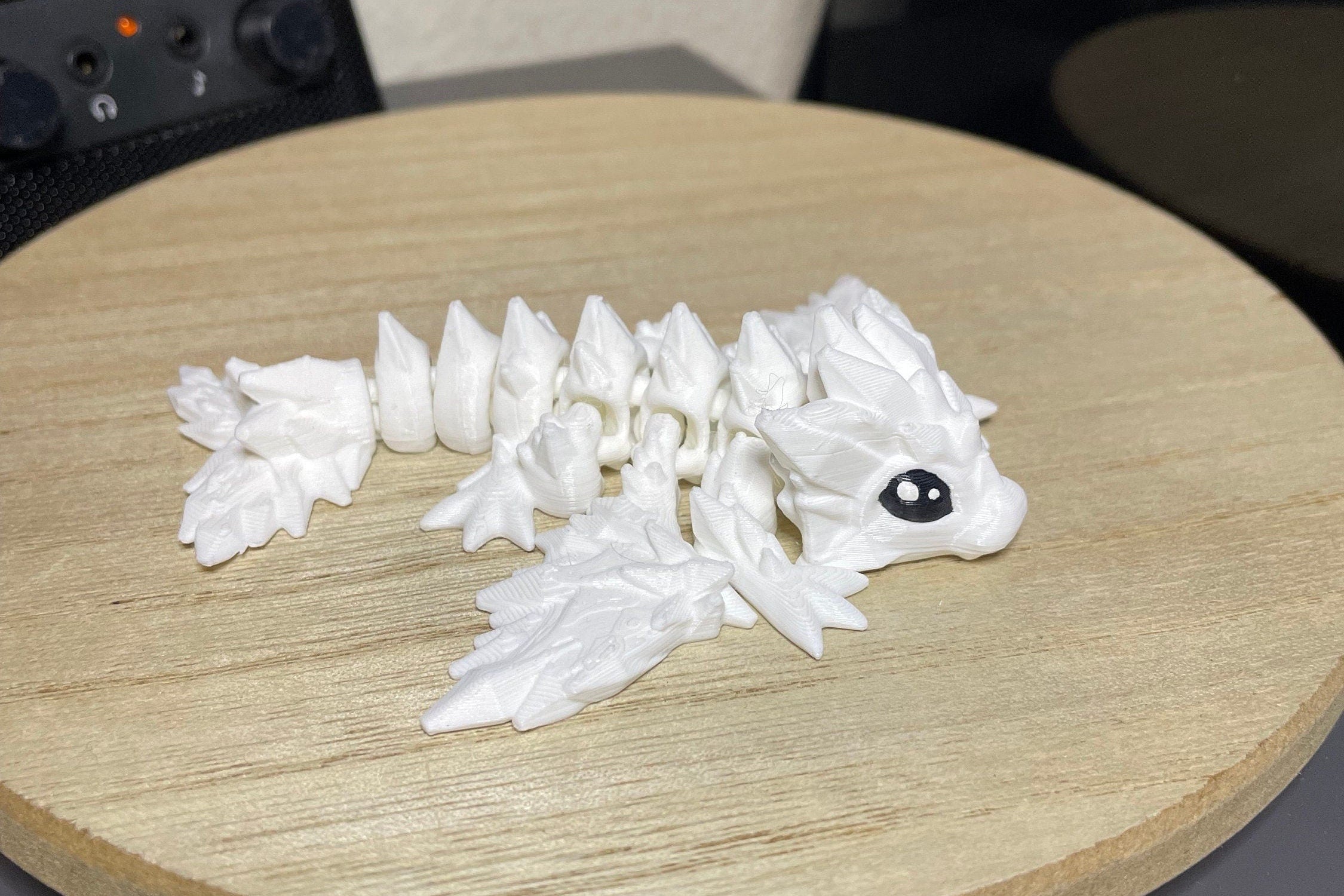 small White dragon model on a wooden surface, with cute black painted eyes with white pupils.